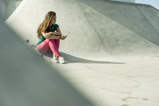 Young Skate Boarder Sitting In A Skatepark Using Smartphone