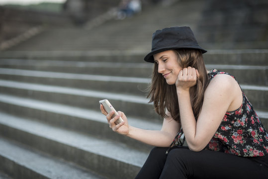 Germany, Koblenz, Deutsches Eck, young woman with cell phone sitting on stairs