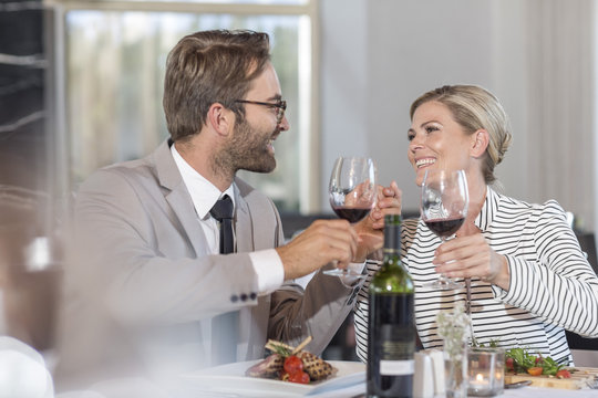 Mid adult couple in restaurant toasting with red wine