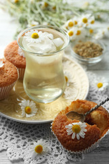 Glass of chamomile tea with chamomile flowers and tasty muffins on color wooden background