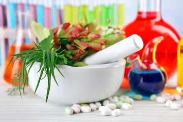Herbs in mortar, test tubes and pills,  on table, on light background