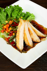 Slices of chicken fillet with sauce and vegetables on table close up