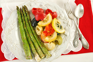 Roasted asparagus and tasty colorful pasta with vegetables on plate on wooden table background