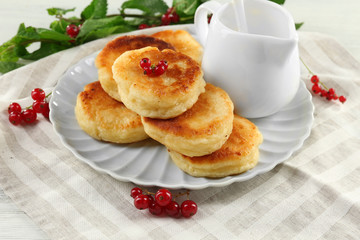 Fritters of cottage cheese with red currant in plate on table, closeup