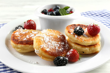 Fritters of cottage cheese with berries in plate on table, closeup