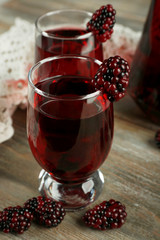 Glasses of blackberry juice on wooden table, closeup