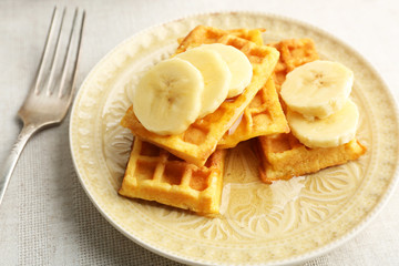 Sweet homemade waffles with sliced banana on plate, on light background