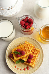 Sweet homemade waffles with fresh raspberries on plate, on light background