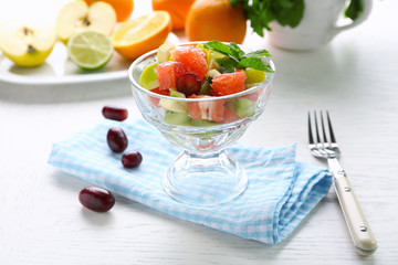 Fruit salad in glass bowl, on light wooden background