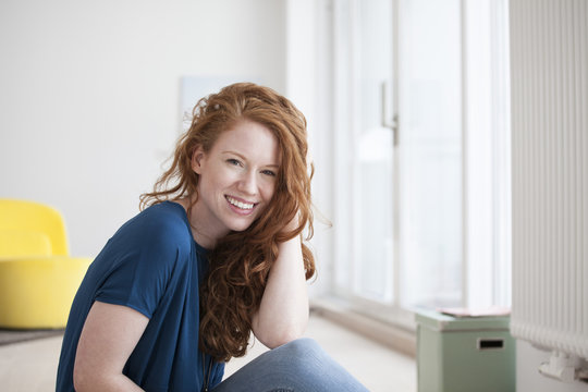 Portrait of happy young woman sitting on the floor of her living room