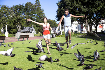 Enthusiastic young couple chasing pigeons in park