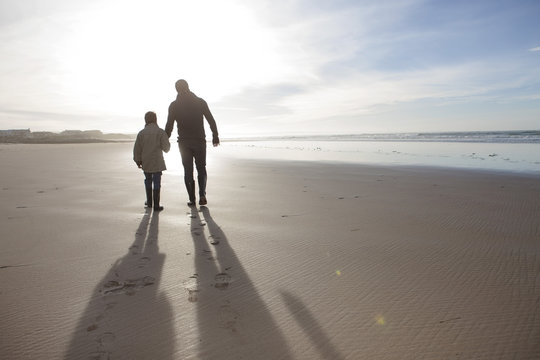 South Africa, Witsand, father and son walking on the beach at backlight