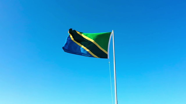 Tanzania flag streaming on clear blue sky background.