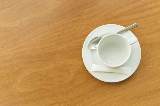 Empty white cup and saucer with a silver spoon and as ache of sugar on a wooden table