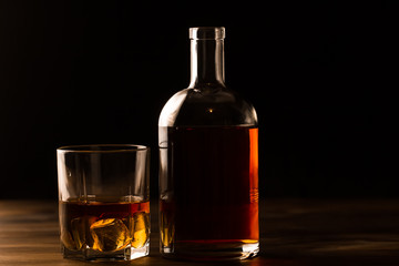 glass of whiskey with ice and a bottle on a wooden table. Cognac, brandy.