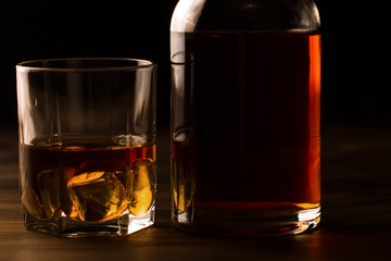 glass of whiskey with ice and a bottle on a wooden table. Cognac, brandy.