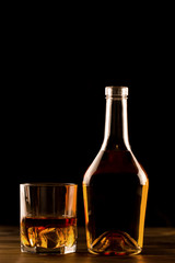 glass of whiskey with ice and a bottle on a wooden table. Cognac, brandy.