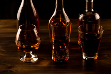 glass of whiskey with ice and a bottle on a wooden table. Cognac, brandy.