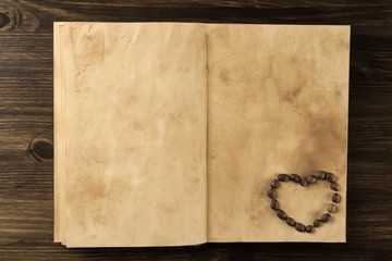 roasted coffee beans in shape of heart on old vintage open book. Menu, recipe, mock up. Wooden background.