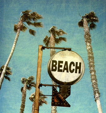 aged and worn vintage photo of beach sign with arrow and palm trees