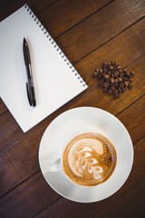 Cup of cappuccino with coffee art and notepad