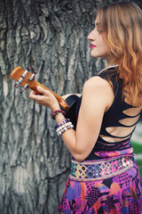 Obraz premium Young Lady Hippie Girl with Red Hair Playing Music on Ukulele Small Guitar Outdoor