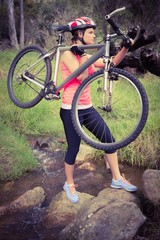 Blonde athlete carrying her mountain bike over stream