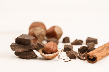 Broken chocolate bar, hazelnut and cinnamon on wooden background, close-up