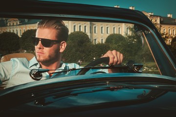 Confident wealthy young man behind classic convertible steering wheel