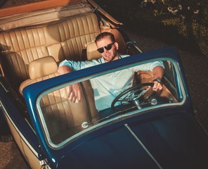 Confident wealthy young man behind classic convertible steering wheel