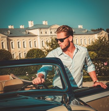 Confident wealthy young man behind classic convertible steering wheel