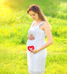 Young pregnant woman with red heart outdoors in sunny summer day