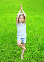 Little girl child on the grass does yoga exercise outdoors in su