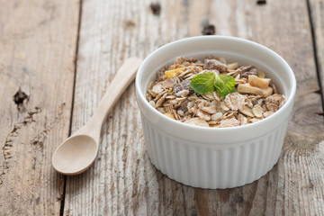 Muesli in white bowl on wood background.