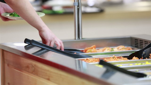 A woman taking vegetables in the salad bar. Lunch in the canteen.