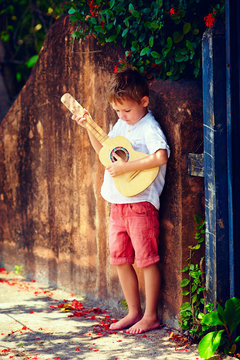 cute young boy playing guitar near the summer old fence