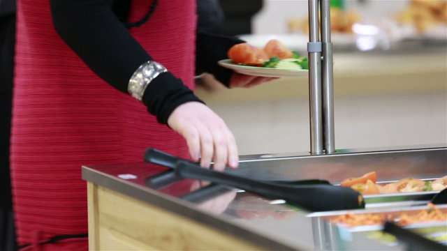 A woman taking vegetables in the salad bar. Lunch in the canteen.