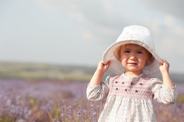Stylish baby girl 2-3 year old walking in lavender field. Wearing rustic dress and hat. Looking at...