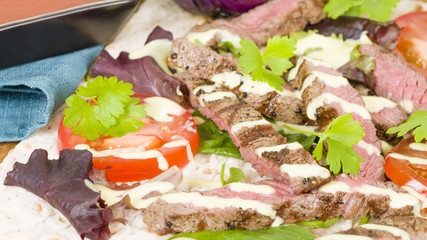 Fototapeta na wymiar Grilled Beef Wraps - Griddled sirloin steak, sliced and wrapped in a flatbread served with blue cheese sauce and salad. Close up. 