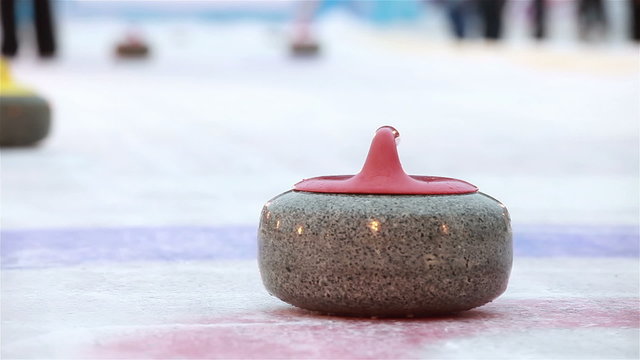 Players curling throw stones on the ice.