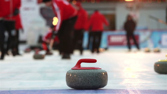 Players curling throw stones on the ice.