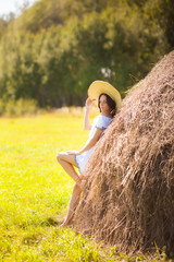 Naklejka na ściany i meble Beautiful girl in a hat stands in haystacks.