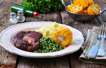 Rare beef steak with mashed potatoes, green peas and boiled corn