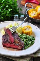 Rare beef steak with mashed potatoes, green peas and boiled corn