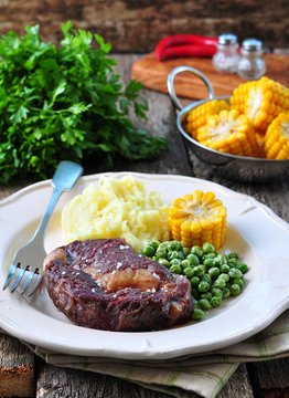 Rare beef steak with mashed potatoes, green peas and boiled corn