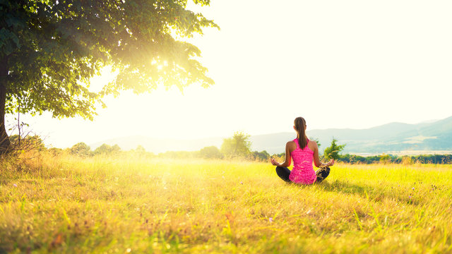 Young athletic woman practicing yoga on a meadow at sunset, image with lens flare