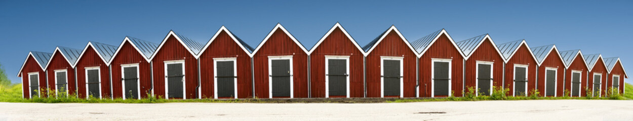 Panoramic view of row of red wooden boathouses