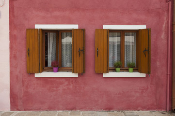 Two windows on a red wall from a colorful house of Burano island