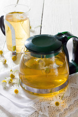 Teapot and cup of herbal tea with chamomile flowers on the woode