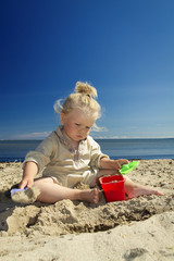 little girl playing in the sand on the beach by the sea